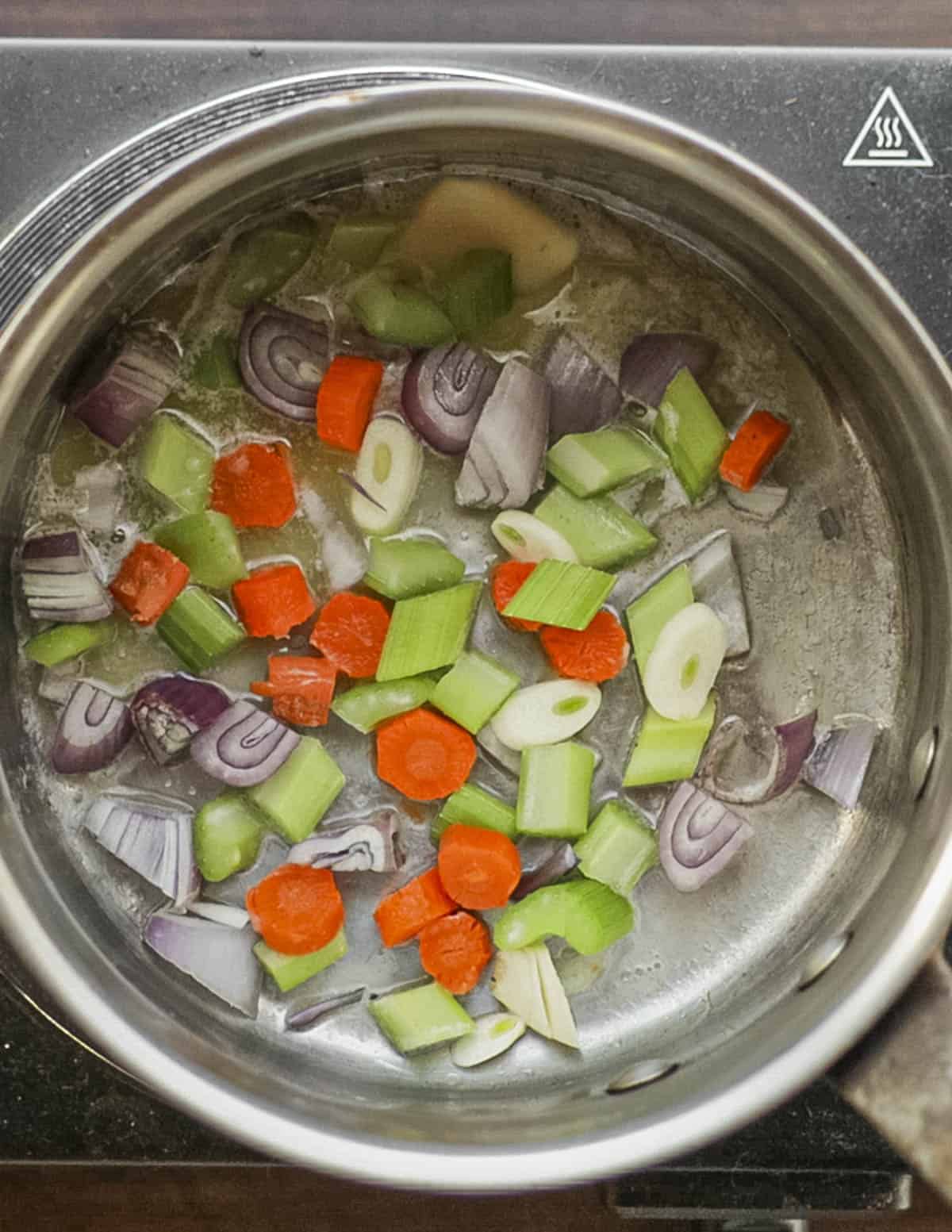 Cooking carrot, garlic, onion and celery in a pot to make marinara. 