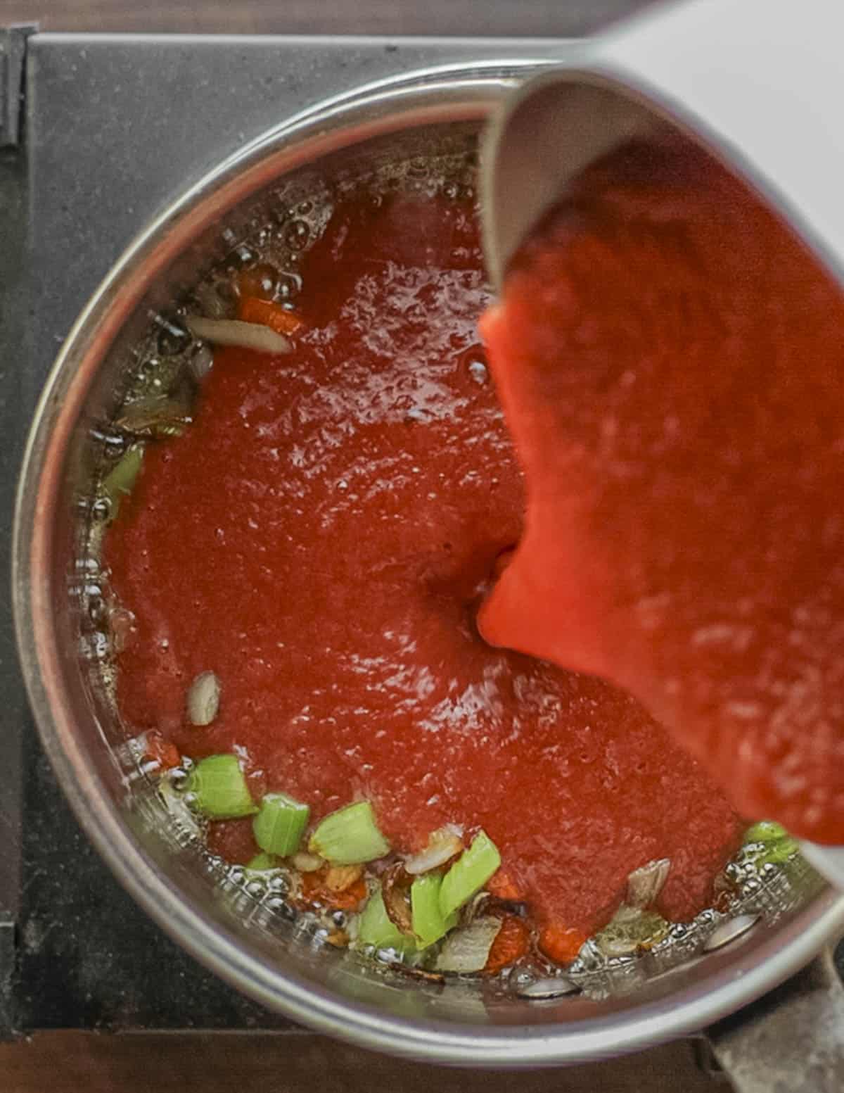 Adding pureed, canned peeled tomatoes to a pot of carrot onion and celery. 