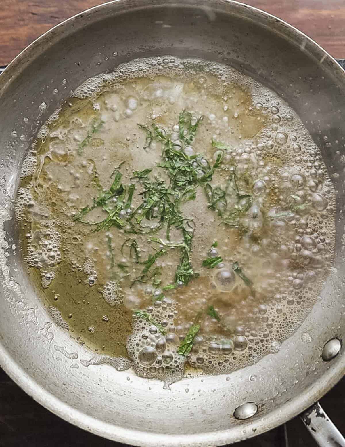 A pan of brown butter sauce with fresh sage or mint leaves and wine. 