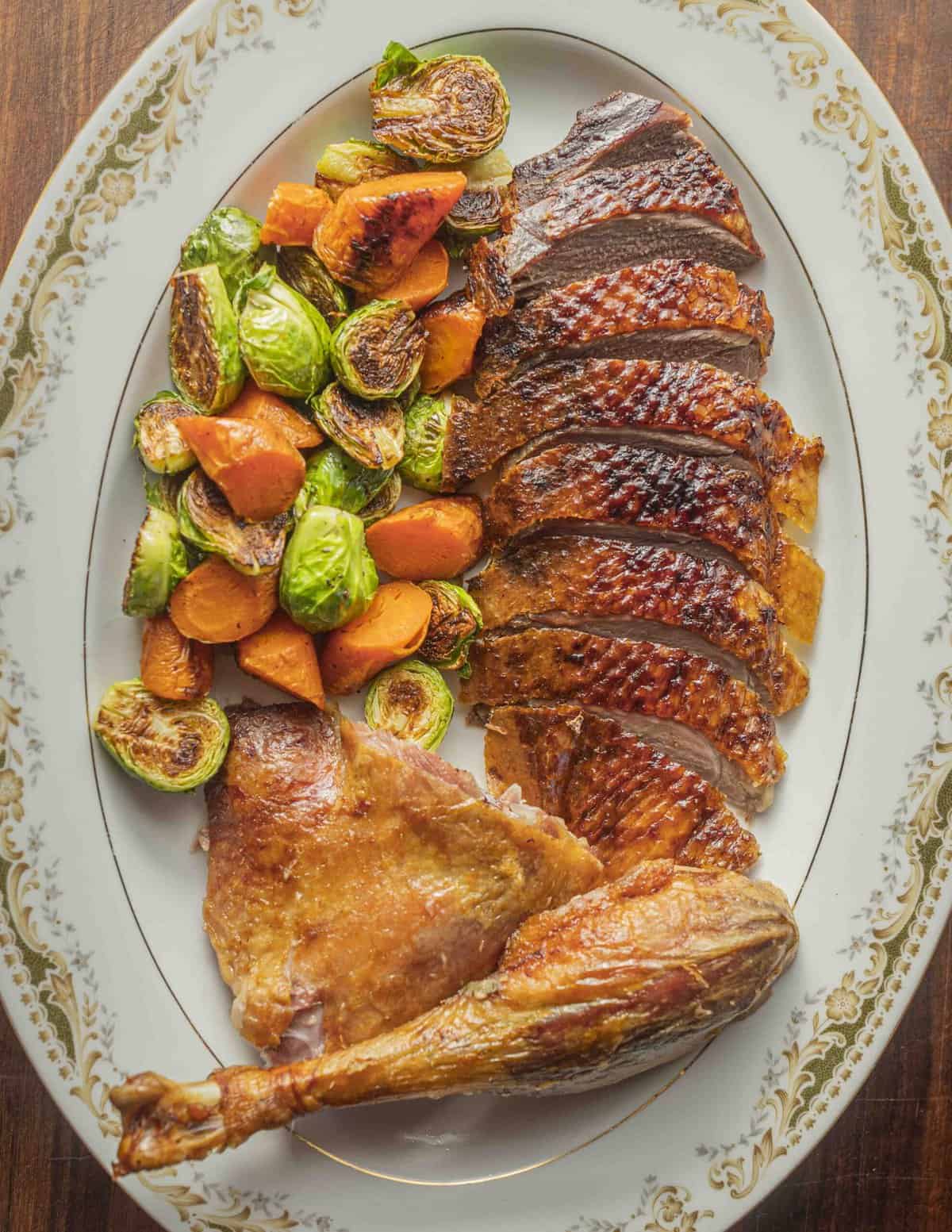 A whole roasted goose cut up on a serving tray with carrots and Brussels Sprouts. 