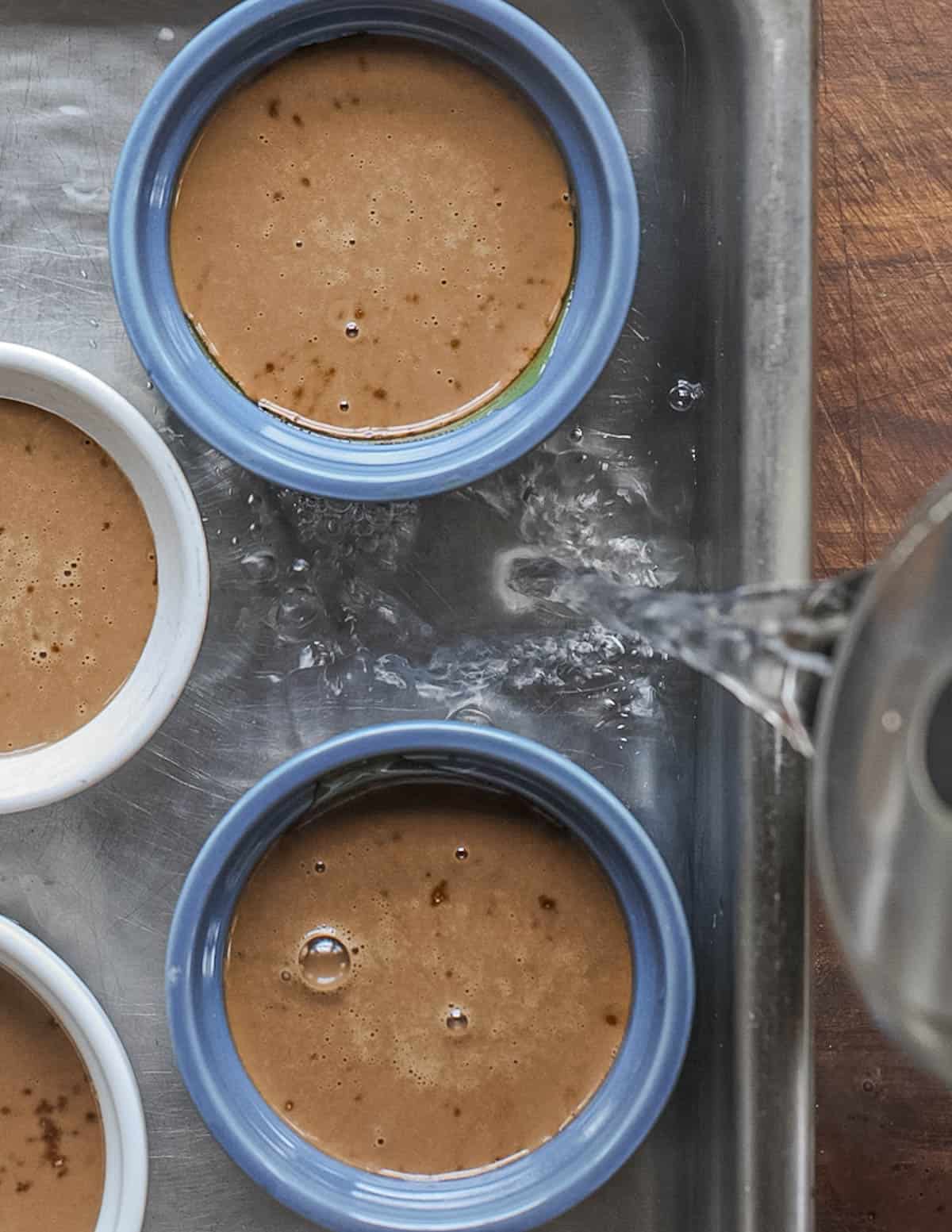 Pouring hot water into a pan of flan ramekins to make a water bath. 