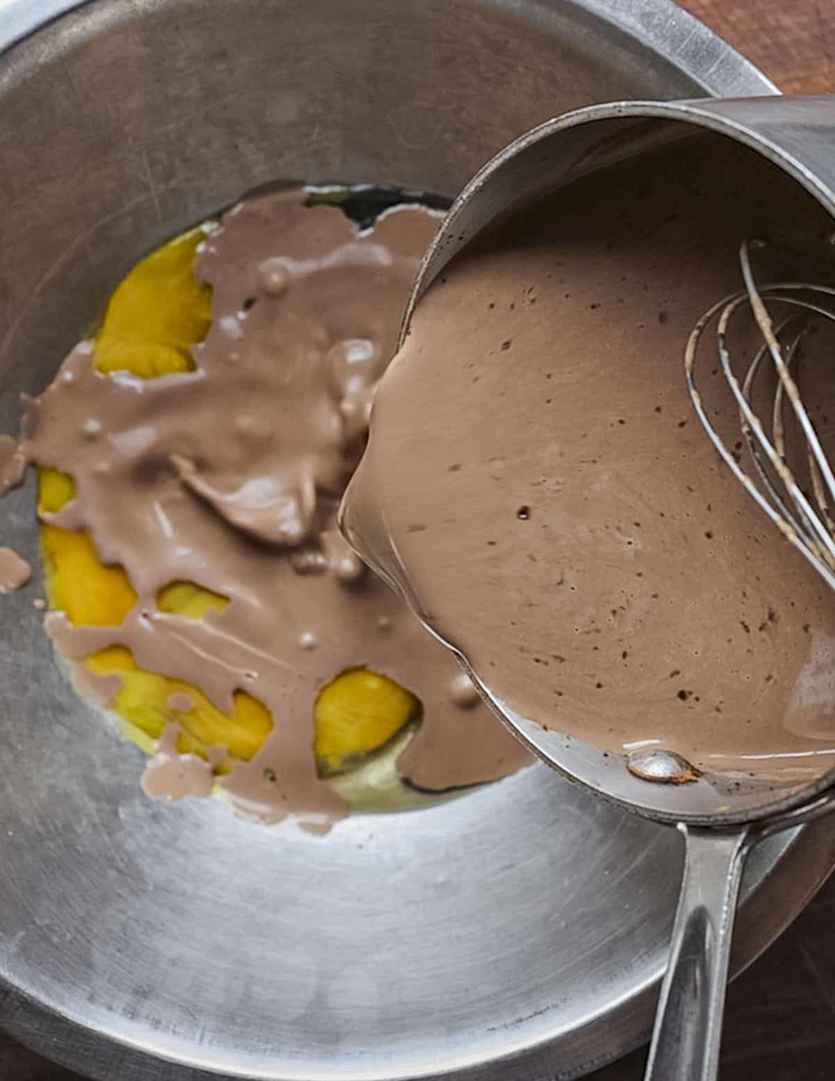 Pouring cooled chocolate cream onto eggs in a bowl. 