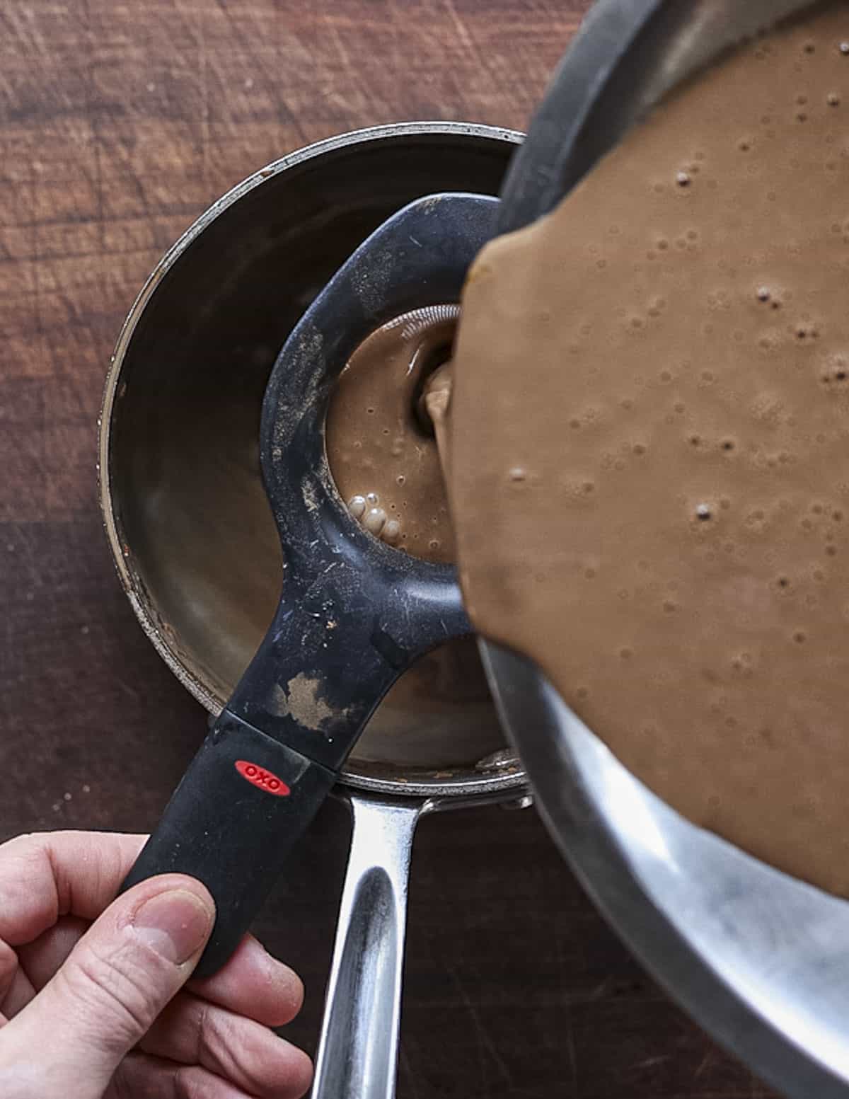 Straining chocolate custard through a sieve before cooking. 