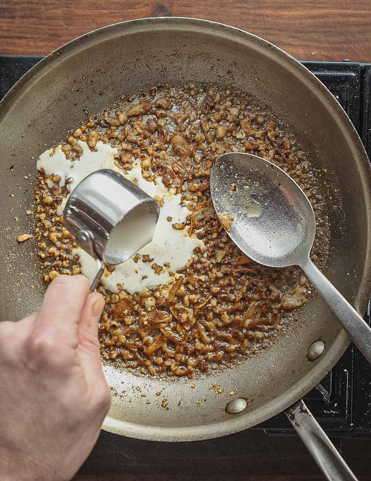 Adding a drizzle of heavy cream to pan of walnuts cooked with garlic. 