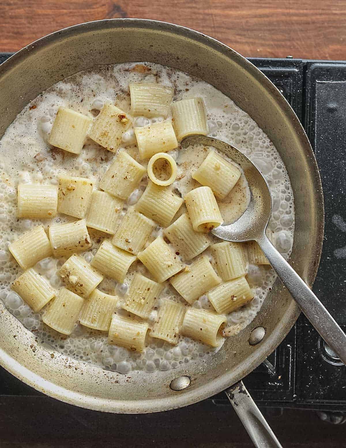 Simmering pasta in a creamy walnut sauce in a pan. a