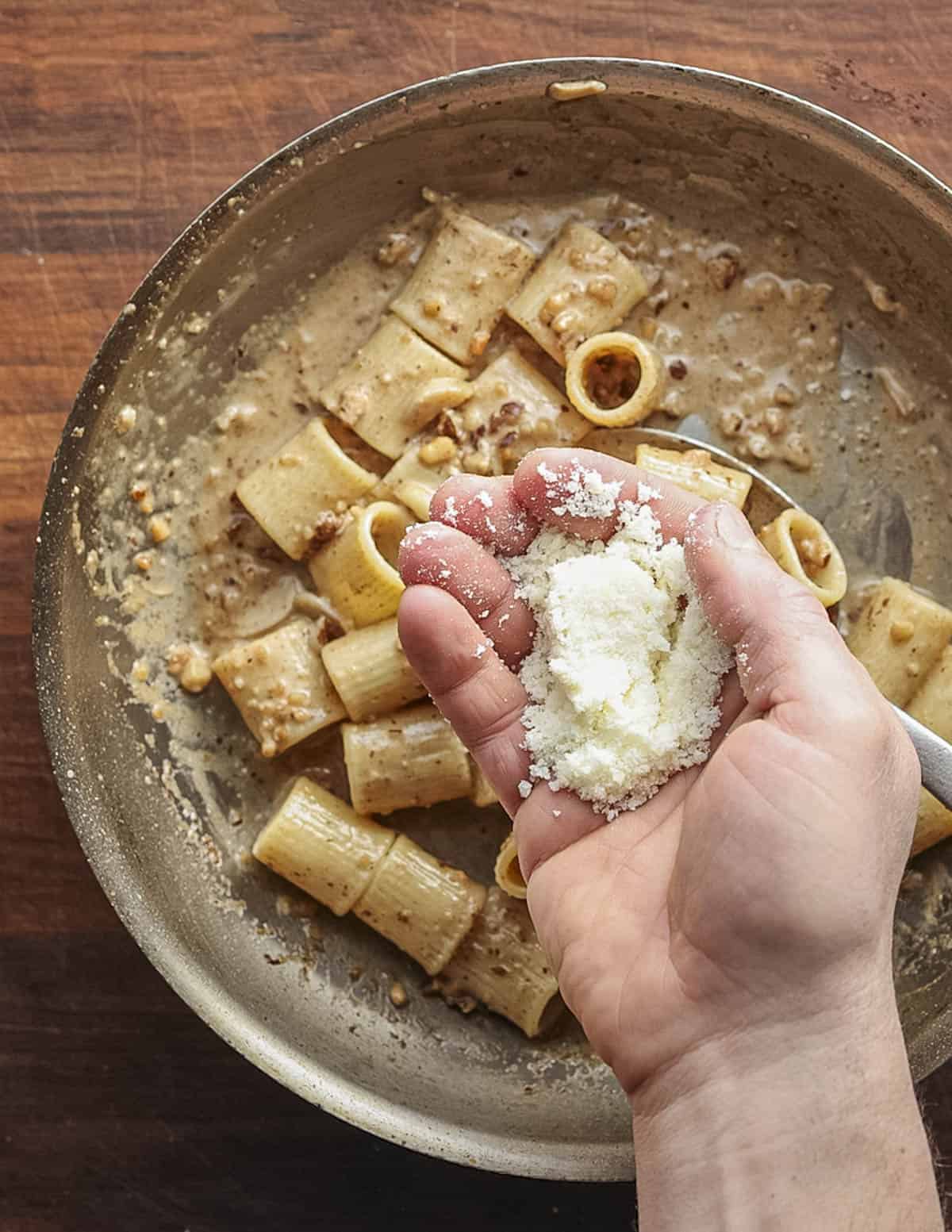 Adding a handful of parmesan cheese to a pan of mezze maniche pasta with walnut sauce.