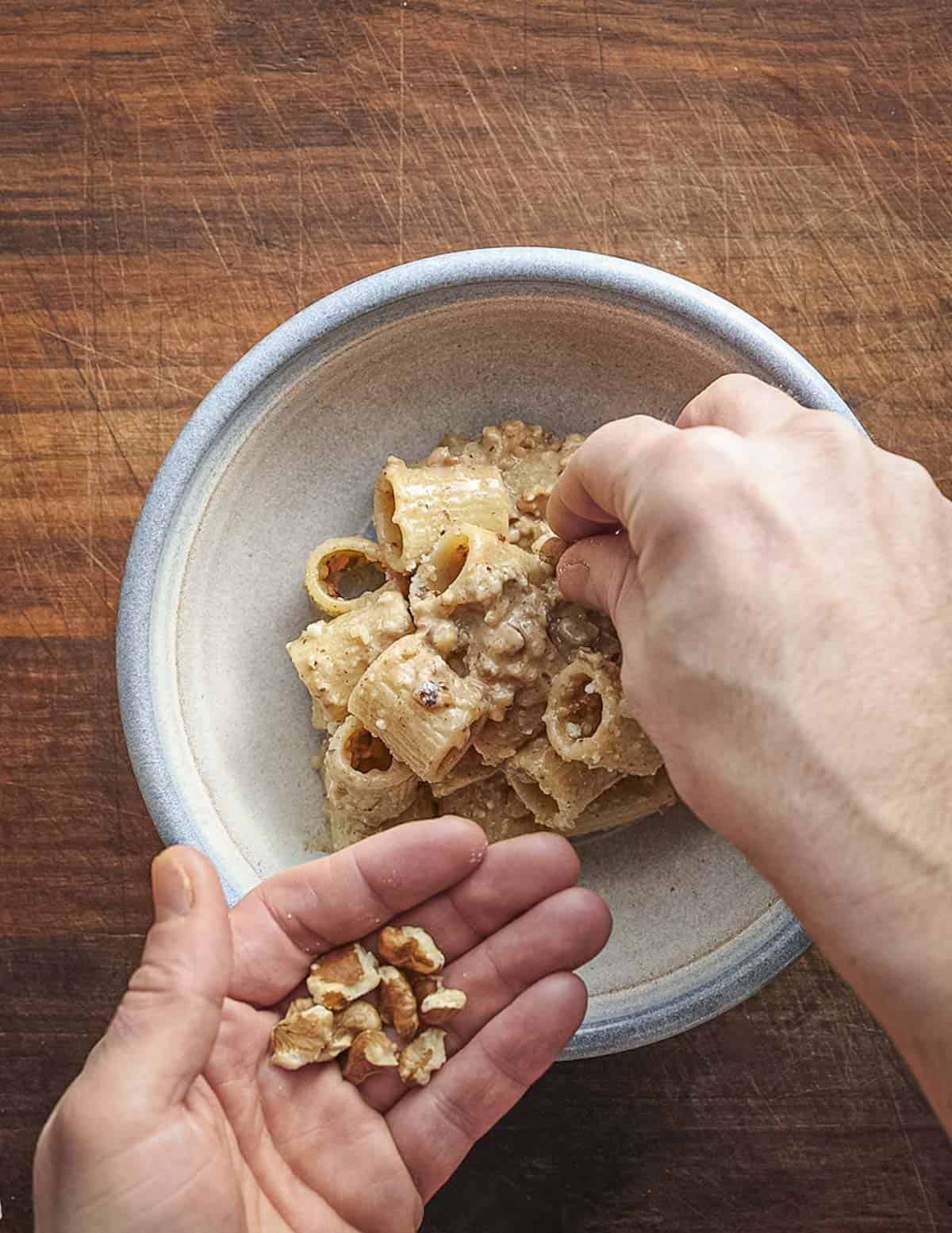 Garnishing a bowl of finished pasta with walnut sauce with freshly cracked black walnuts. 