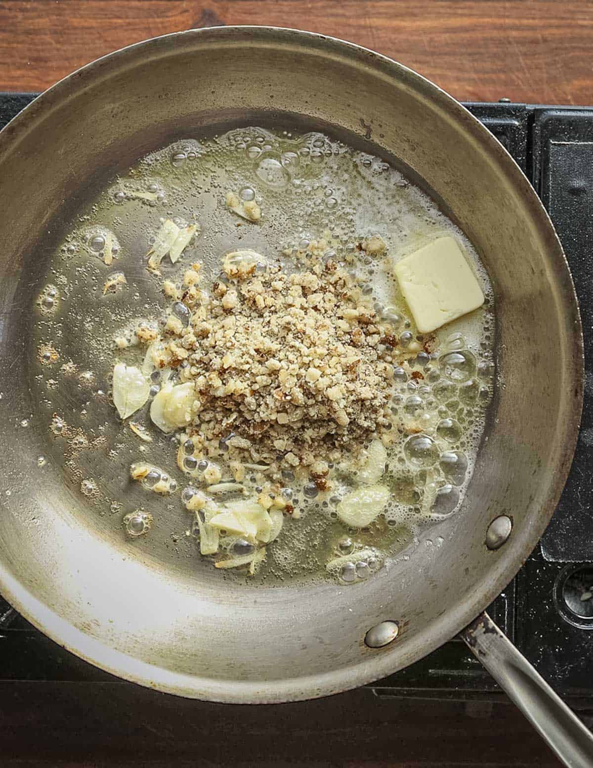 Adding ground crushed walnuts to a pan of garlic and butter.