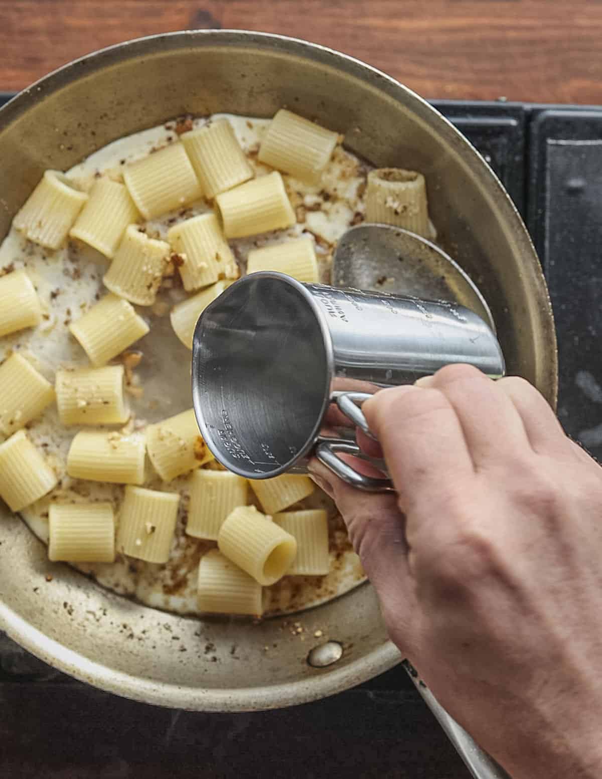 Adding water to a pan in order to finish cooking pasta. 