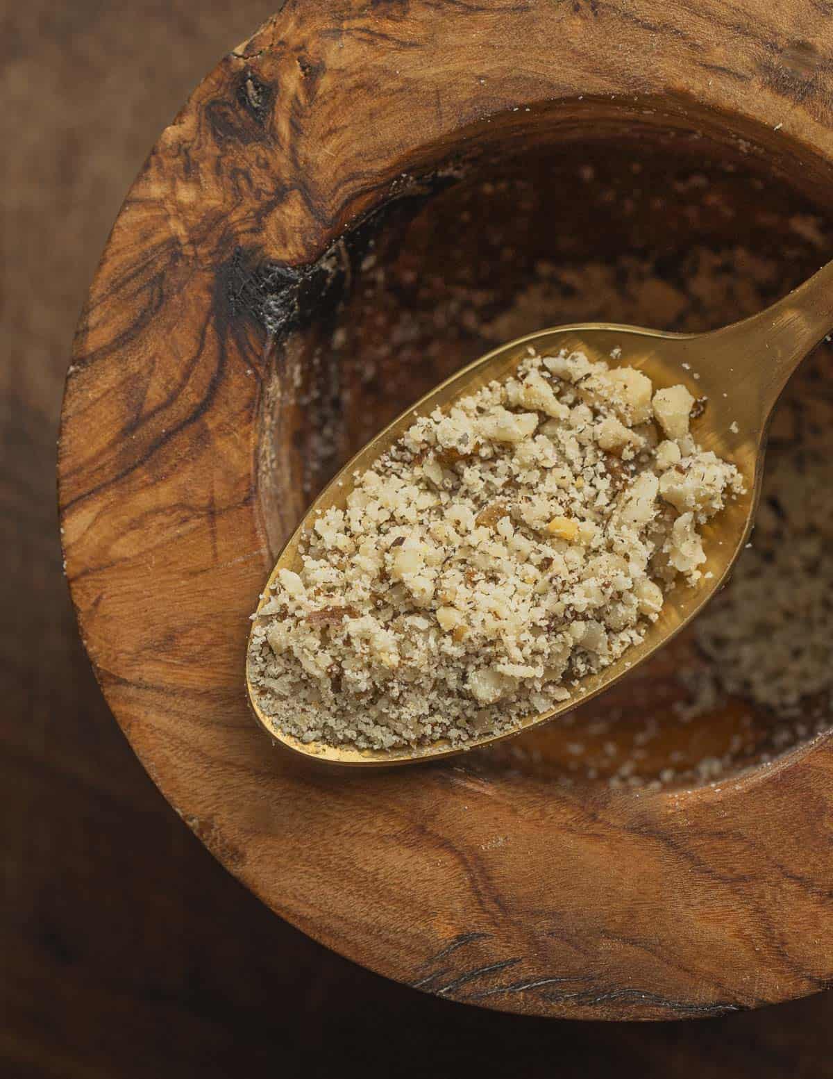 A close up image of a spoon filled with crushed walnuts showing the perfect consistency and texture to make walnut sauce. 