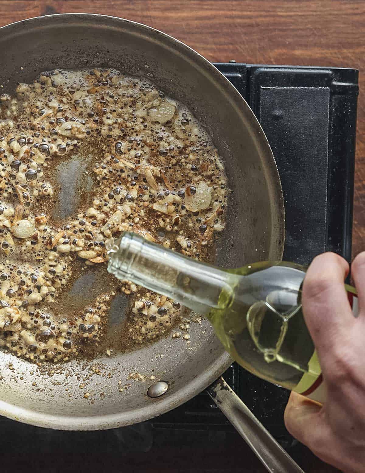 Deglazing a pan of cooking walnuts and garlic with dry white wine.