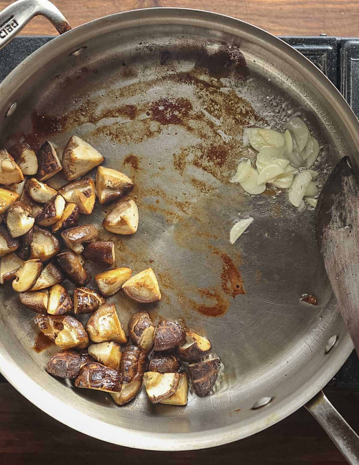 Adding sliced garlic to a pan of cooked mushrooms. 