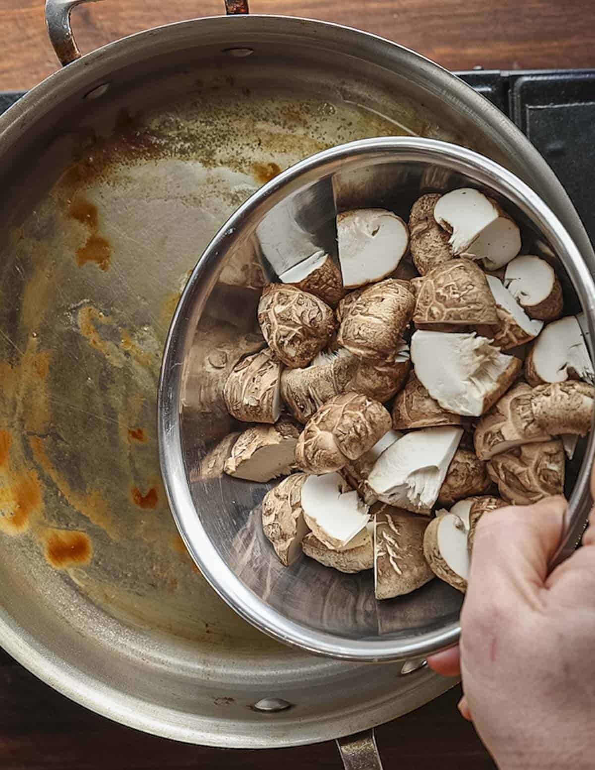 Adding sliced shiitake mushrooms to a pan of sausage drippings. 