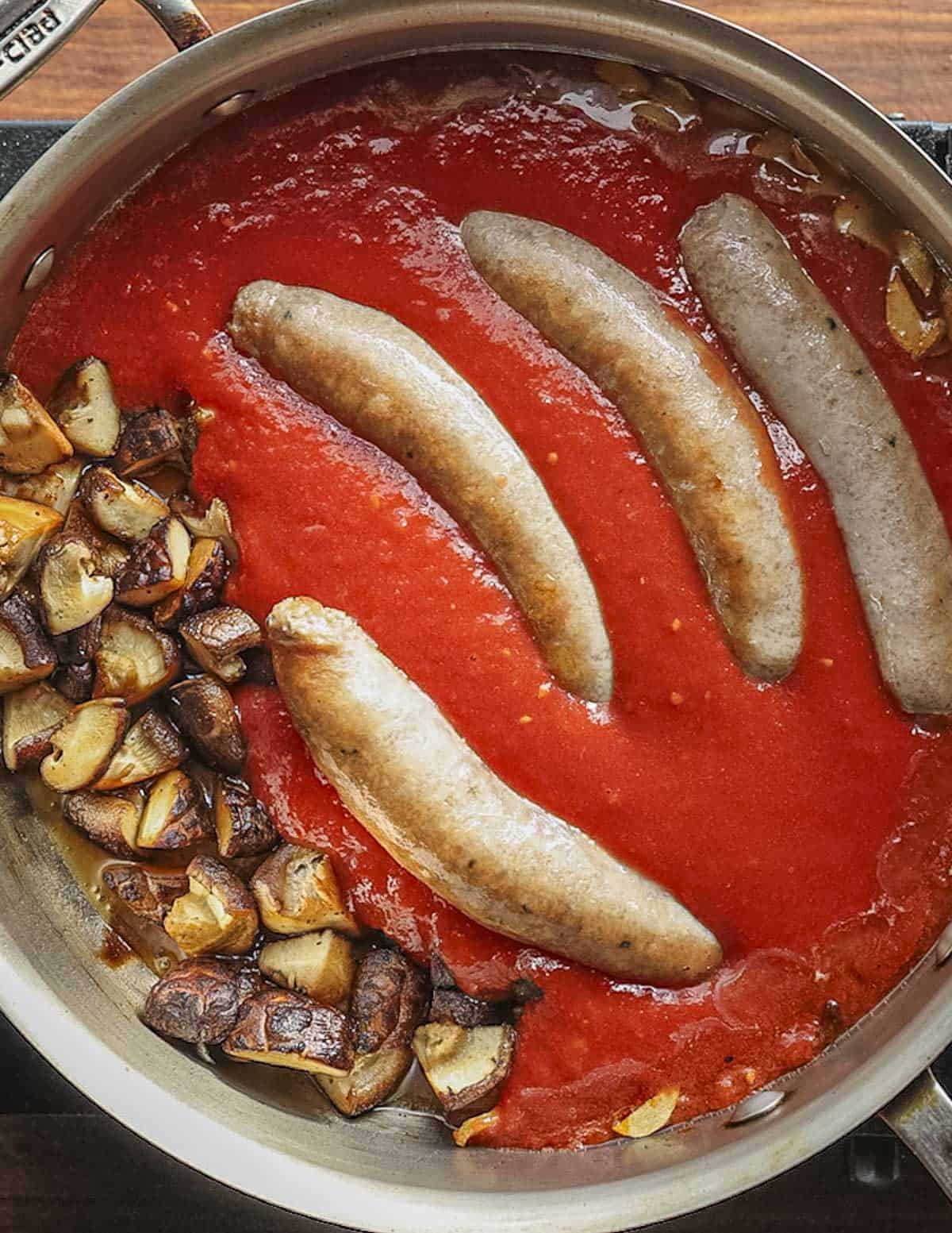 Adding browned sausages to a pan of mushrooms and tomato sauce.