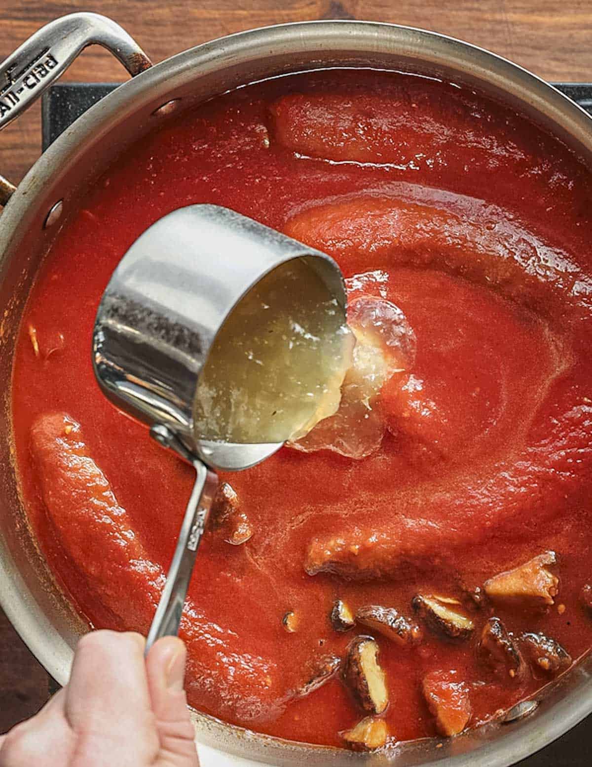 Adding chicken stock to a pan of mushrooms, sausage  and tomato sauce. 