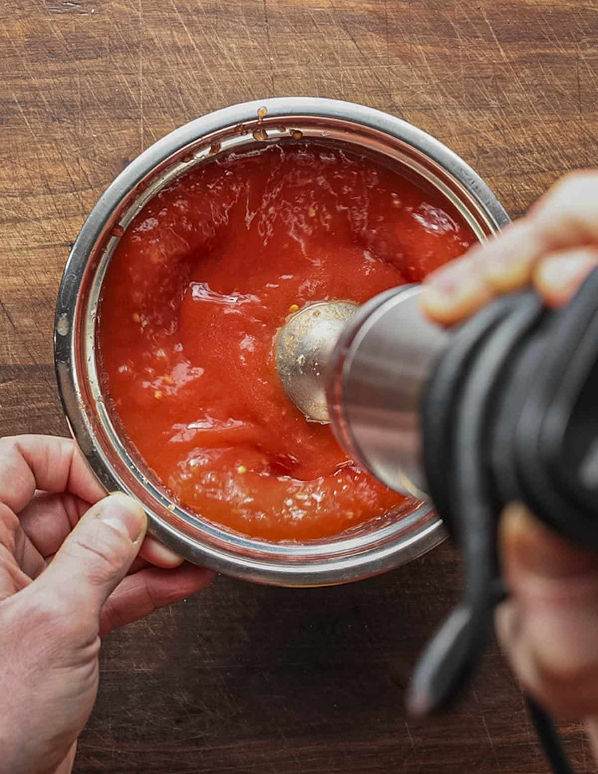 Pureeing canned whole peeled tomatoes with a hand blender. 