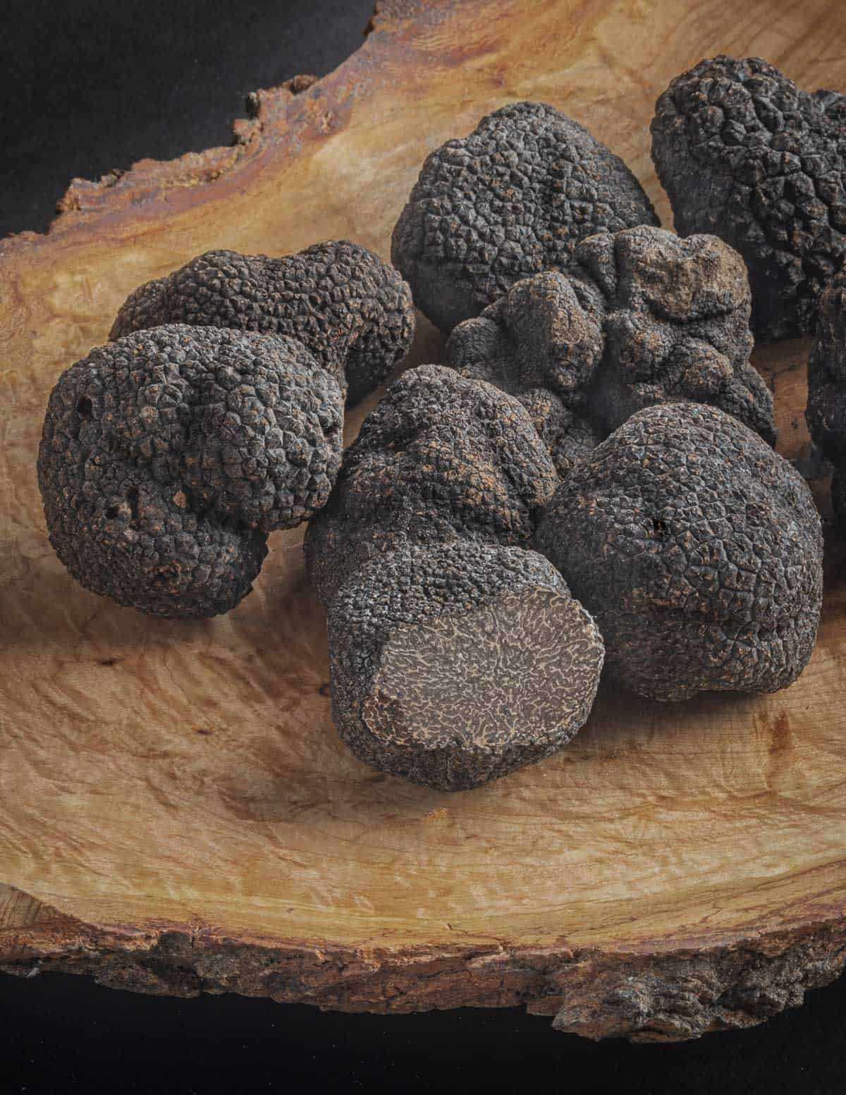 A burl plate with many winter black truffles (Tuber melanosporum) cut showing the inner spore surface with a red tint. 