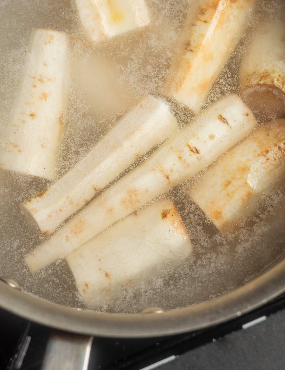 Cooking peeled white salsify roots in white court bouillon. 