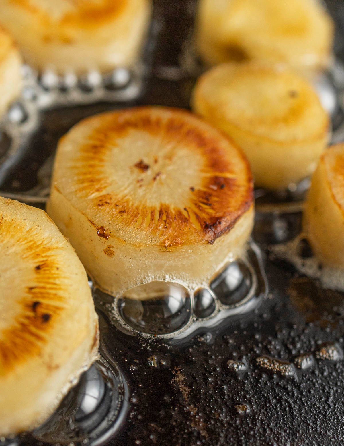 Sliced rounds of salsify root cooking golden brown in a carbon steel pan. 