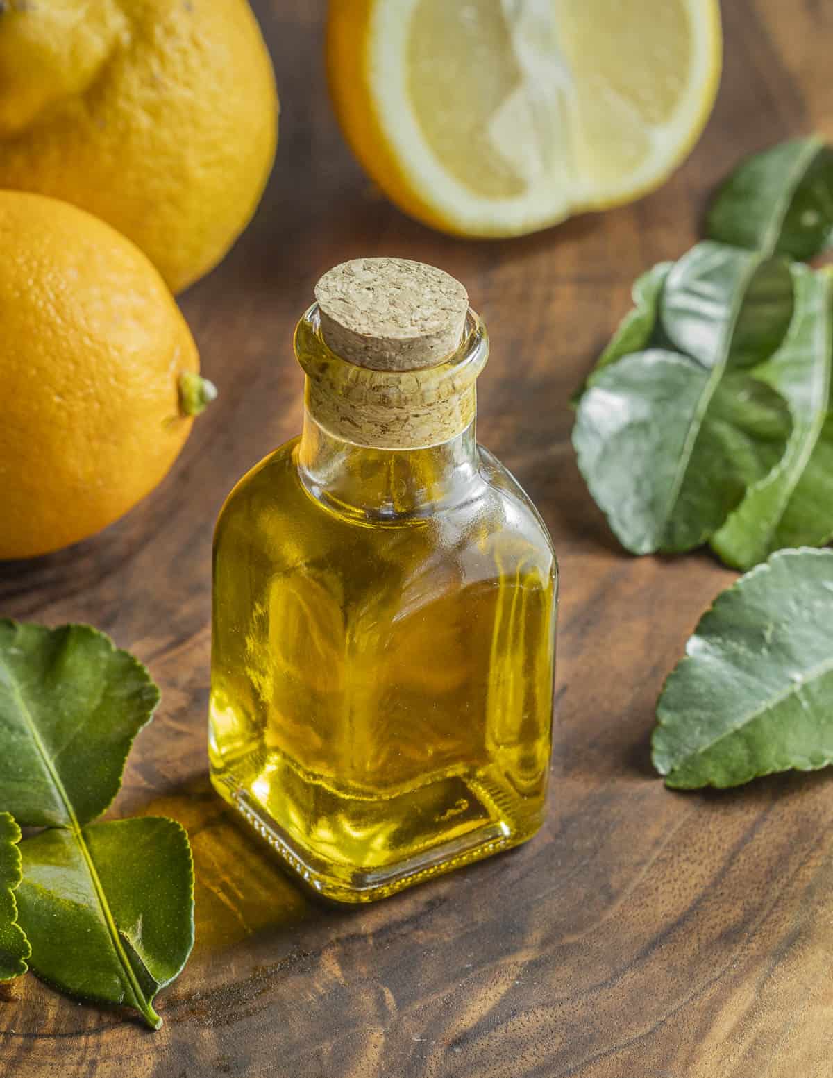 A jar of homemade agrumato or lemon olive oil surrounded by meyer lemons, lemon leaves and fresh lemons. 