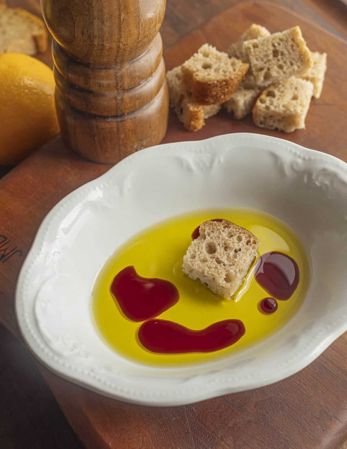 A small dish with lemon olive oil and sweetened raspberry vinegar with a cube of bread being dipped in it. 