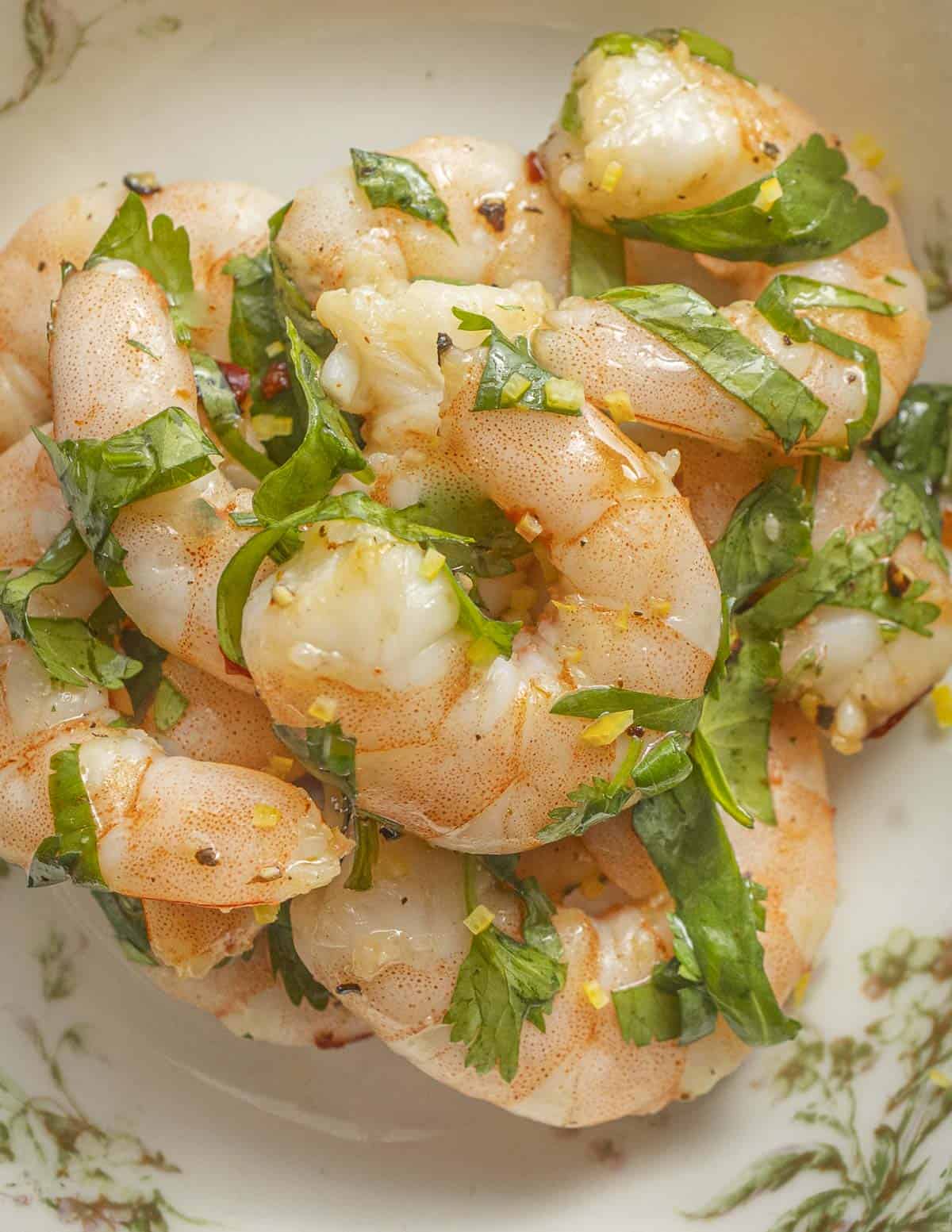 A bowl of cooked marinated shrimp with herbs, lemon oil, red pepper flakes and meyer lemon zest. 