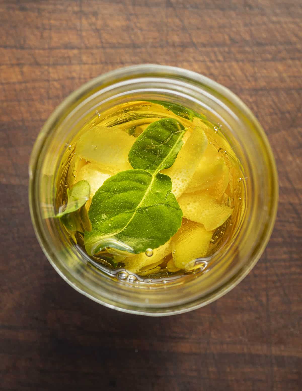 A jar of lemon zest and lemon leaves covered with olive oil.