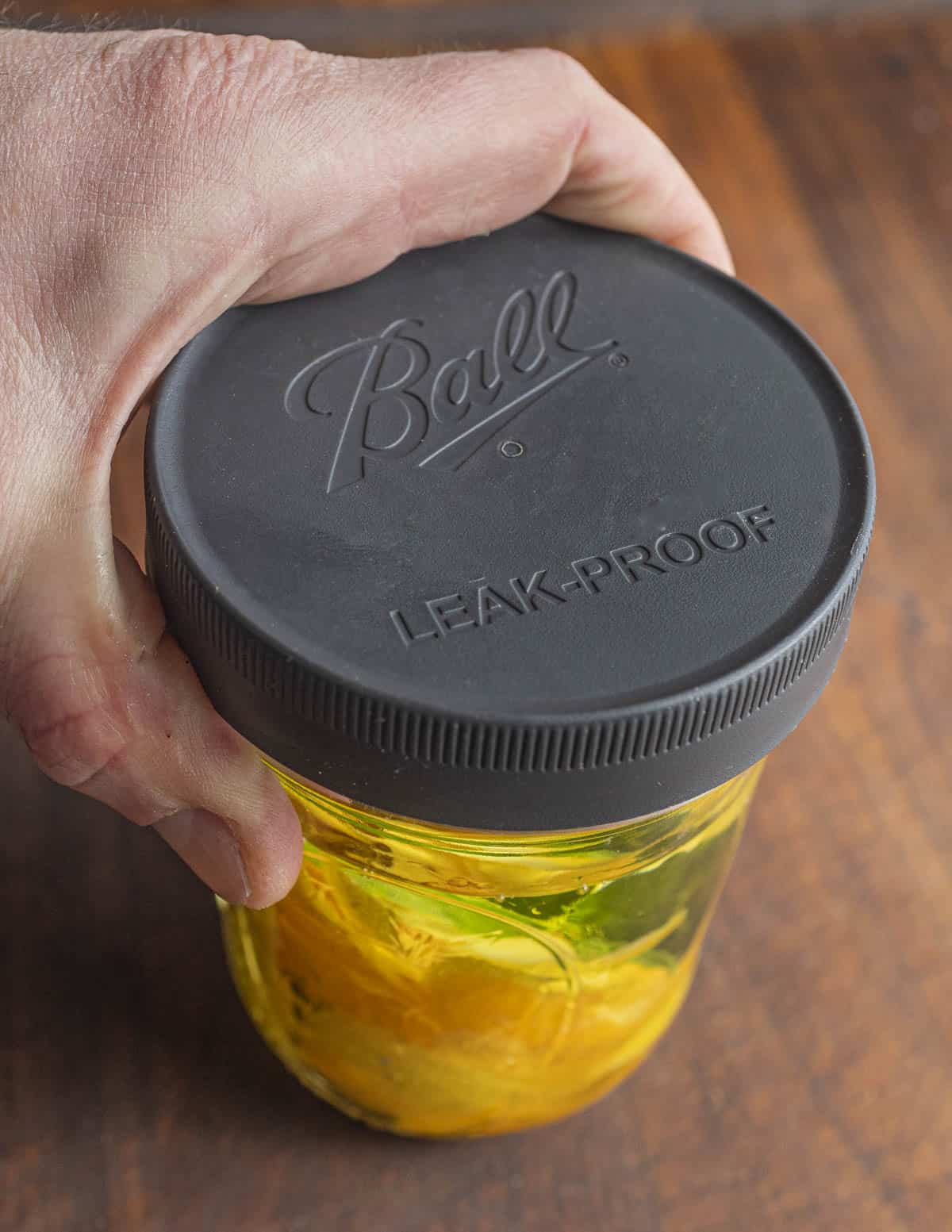 Screwing on a tight-fitting lid onto a jar of lemon zest and olive oil. 