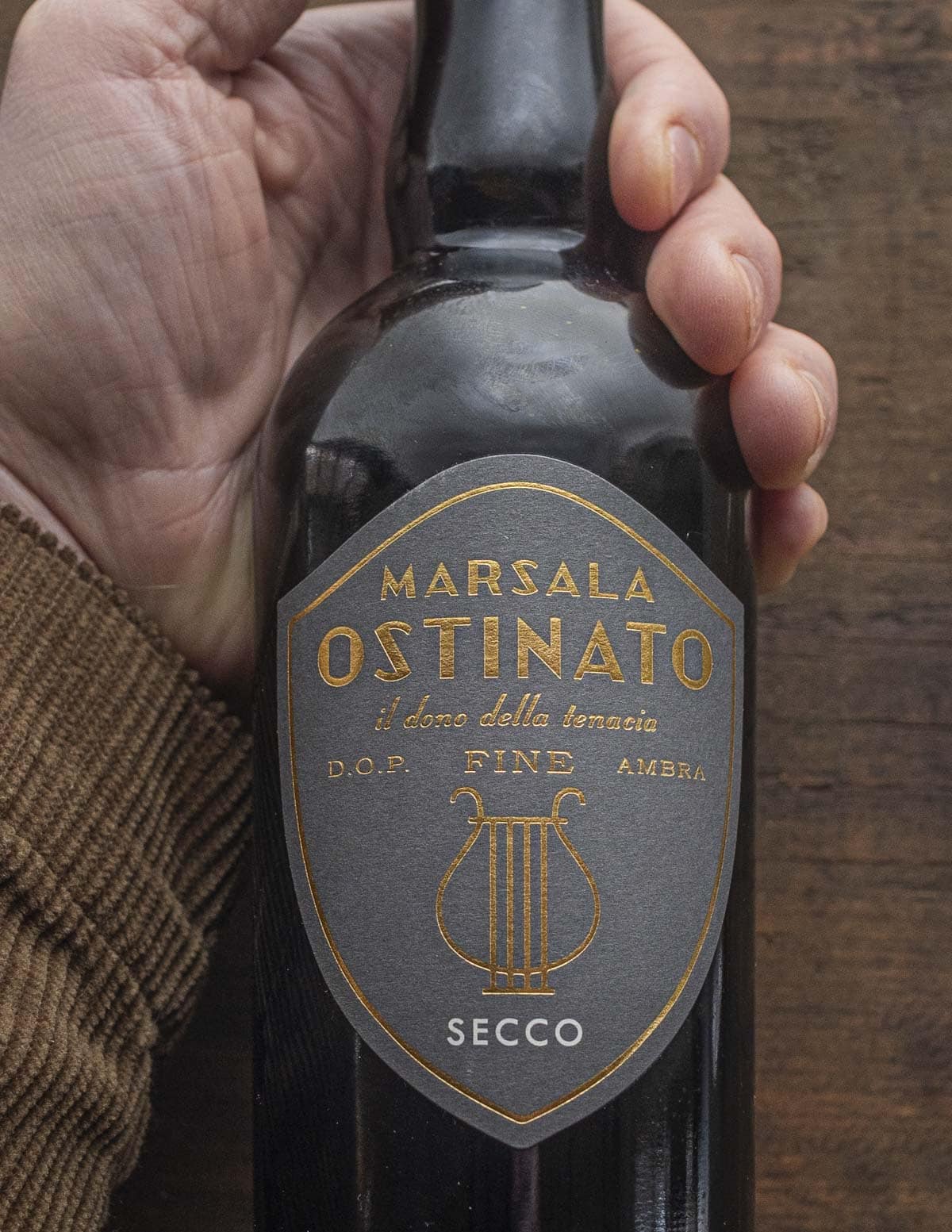 A hand holding a bottle of dry marsala wine. 