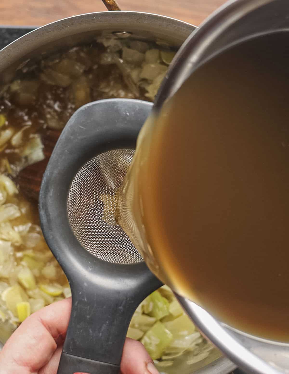 Straining dried mushroom liquid into a pot of soup. 