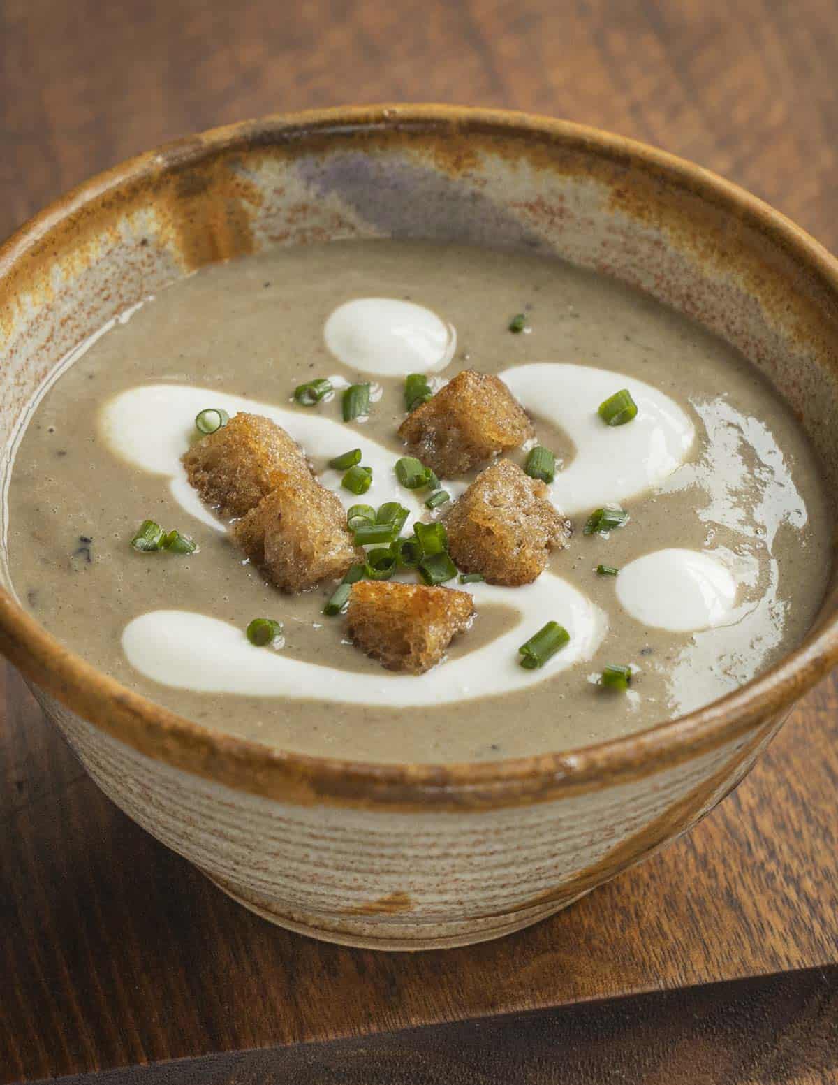 A bowl of cream of mushroom soup with creme fraiche and croutons. 
