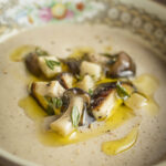 A bowl of cream of mushroom soup garnished with mixed mushrooms, olive oil and fresh thyme.