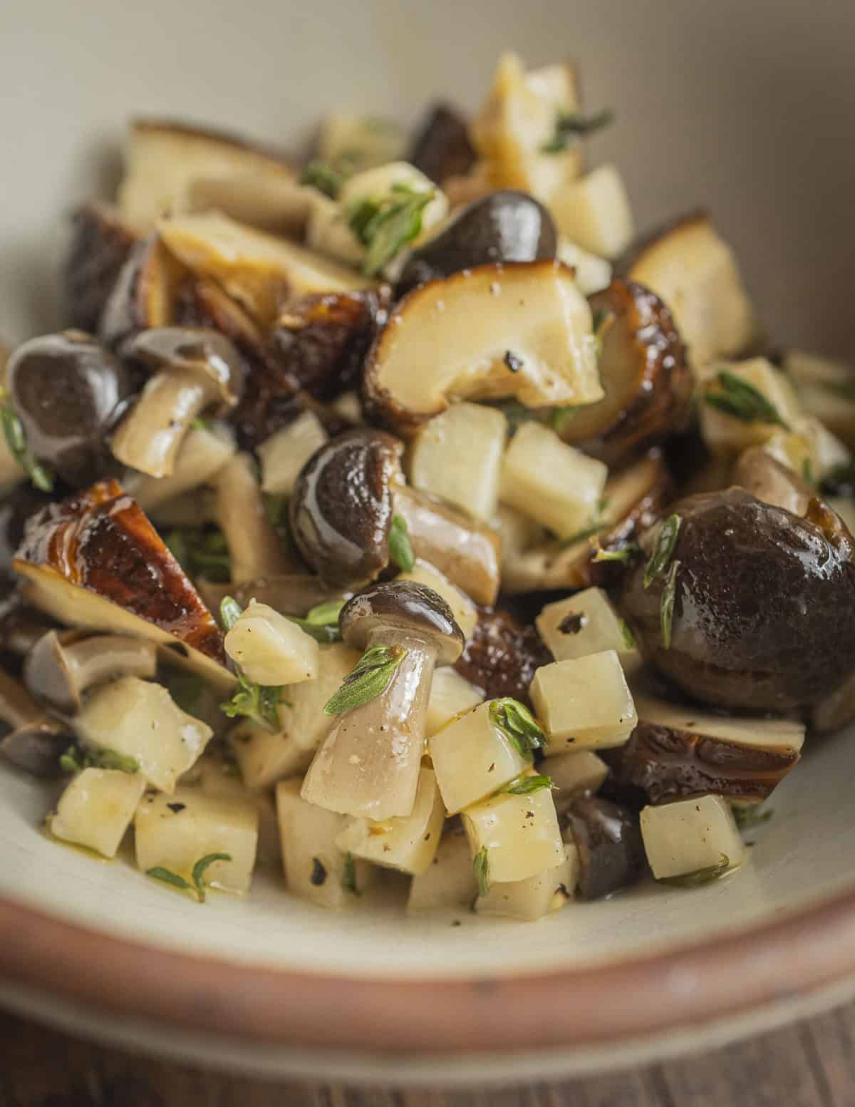 Beech mushrooms, king oyster mushrooms, and shiitake mushrooms cooked in a bowl with olive oil and thyme leaves. 