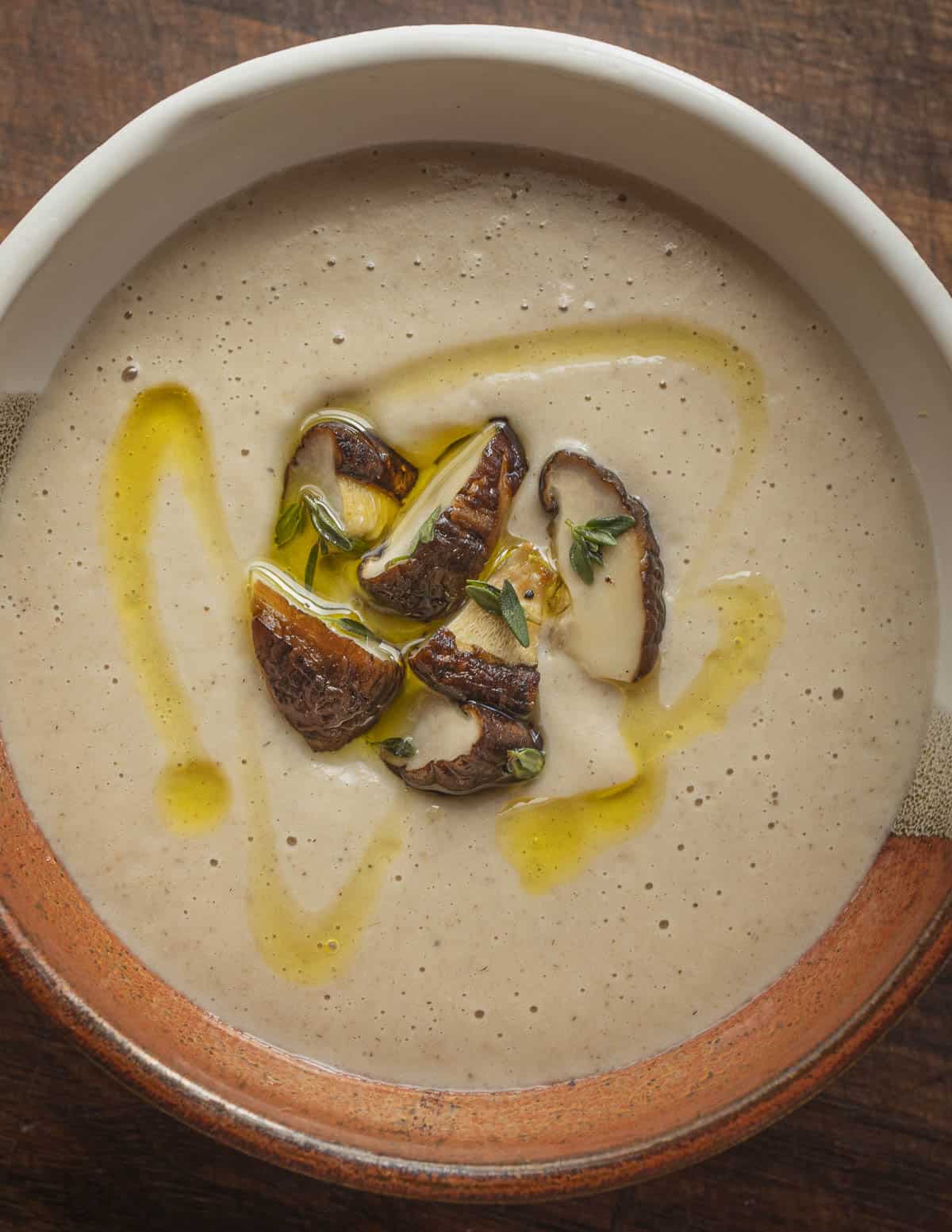 A bowl of roasted garlic shiitake mushroom soup garnished with sliced shiitakes olive oil and thyme. 
