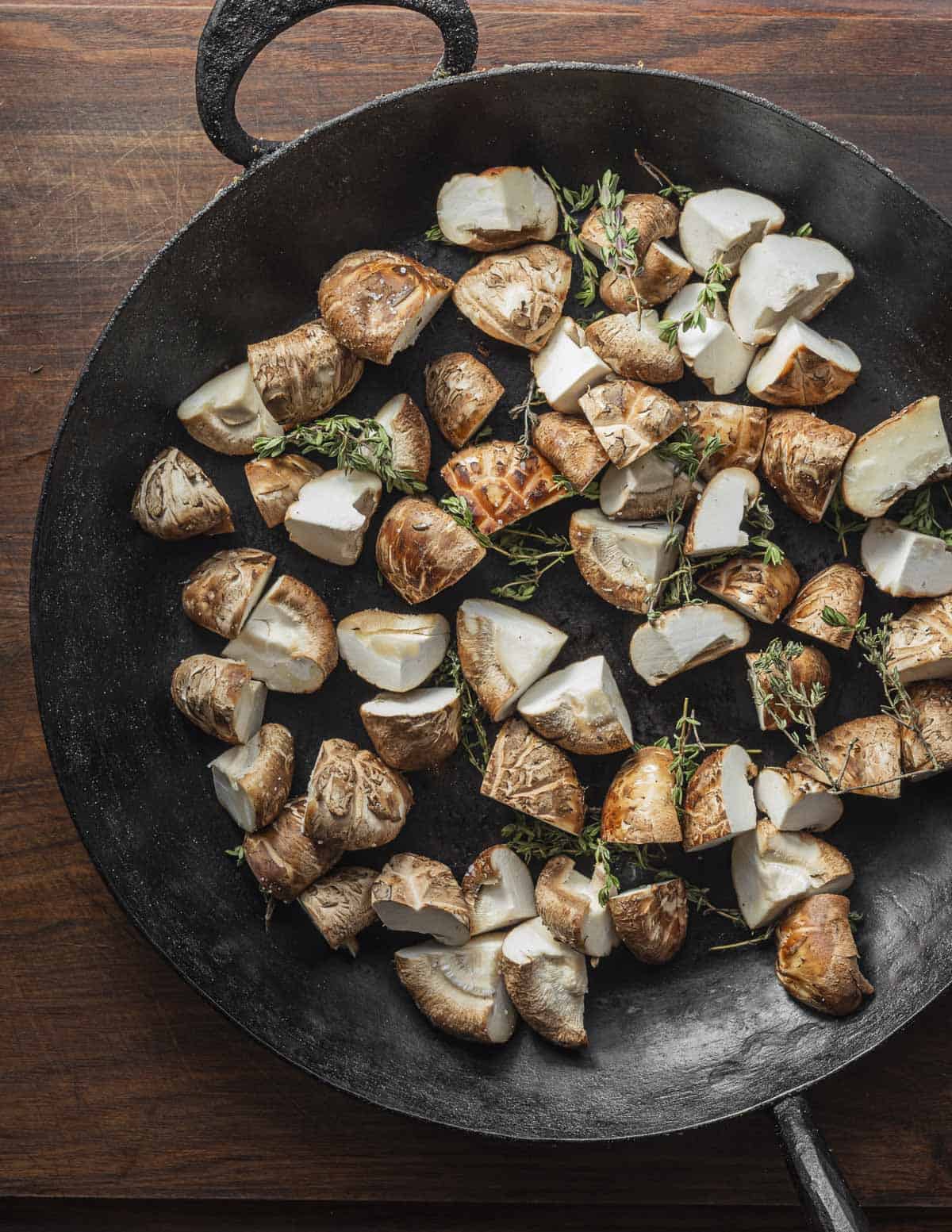 A carbon steel pan with shiitake mushrooms and fresh thyme sprigs ready to cook. 