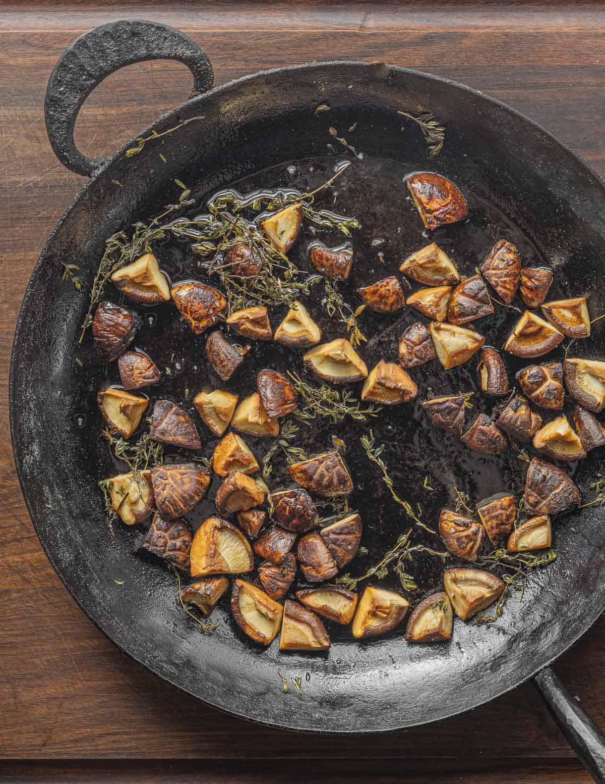 A large carbon steel pan with roasted shiitake mushrooms and fresh thyme sprigs. 