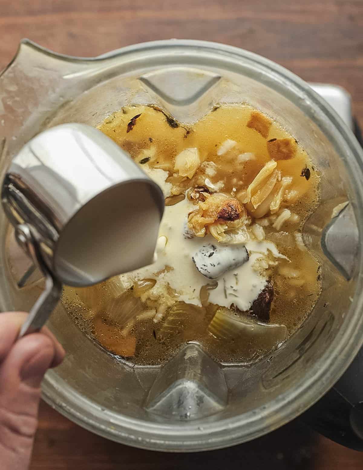 Adding cream to a batch of mushroom soup in a vitamix blender. 