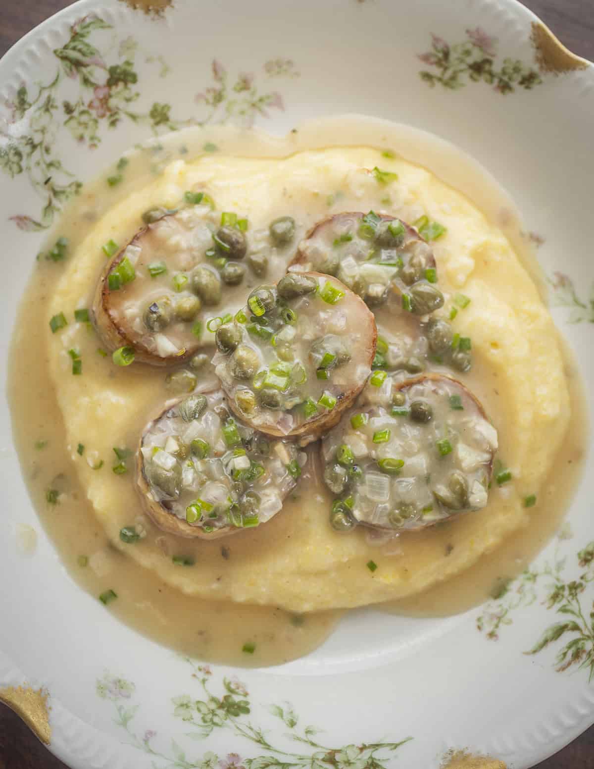 A pan of king oyster mushroom scallops with lemon caper sauce on polenta. 
