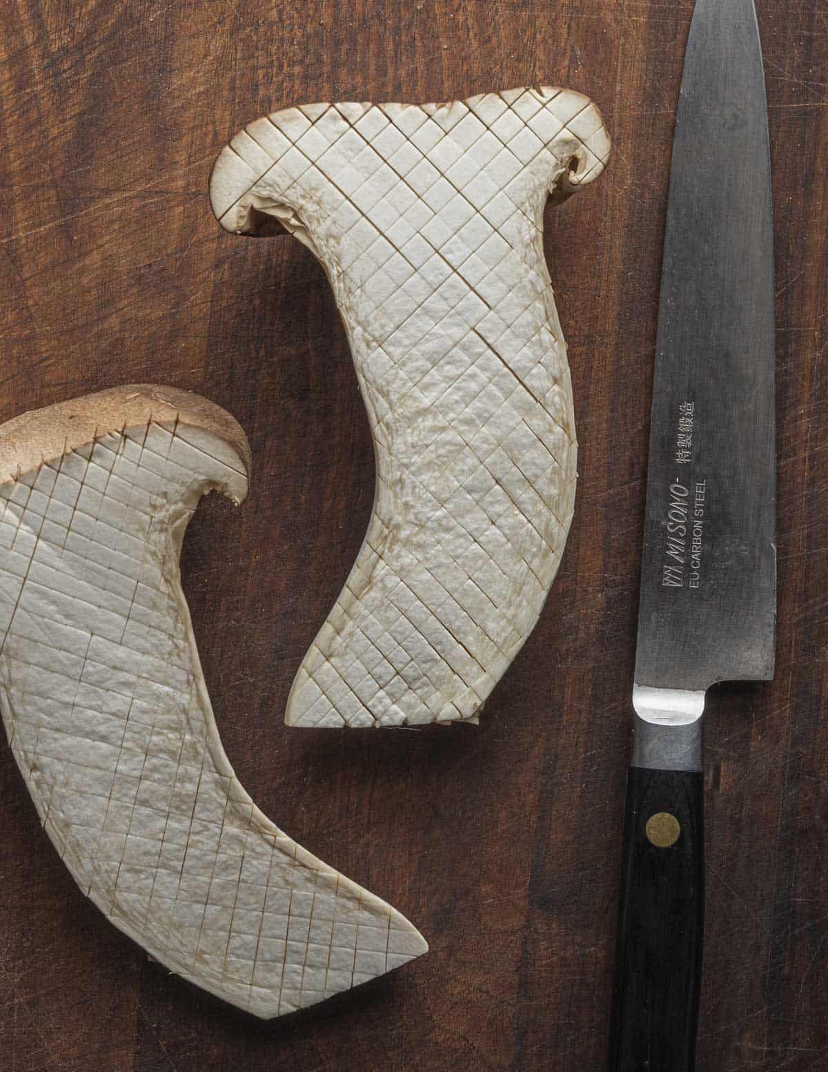 A large king trumpet mushroom cut in half and scored with a cross-hatch pattern using a paring knife. 