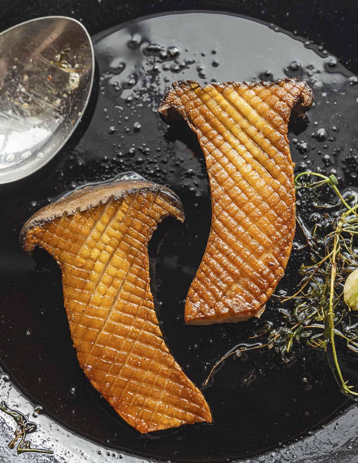 Two golden brown king trumpet mushroom halves in a pan. 