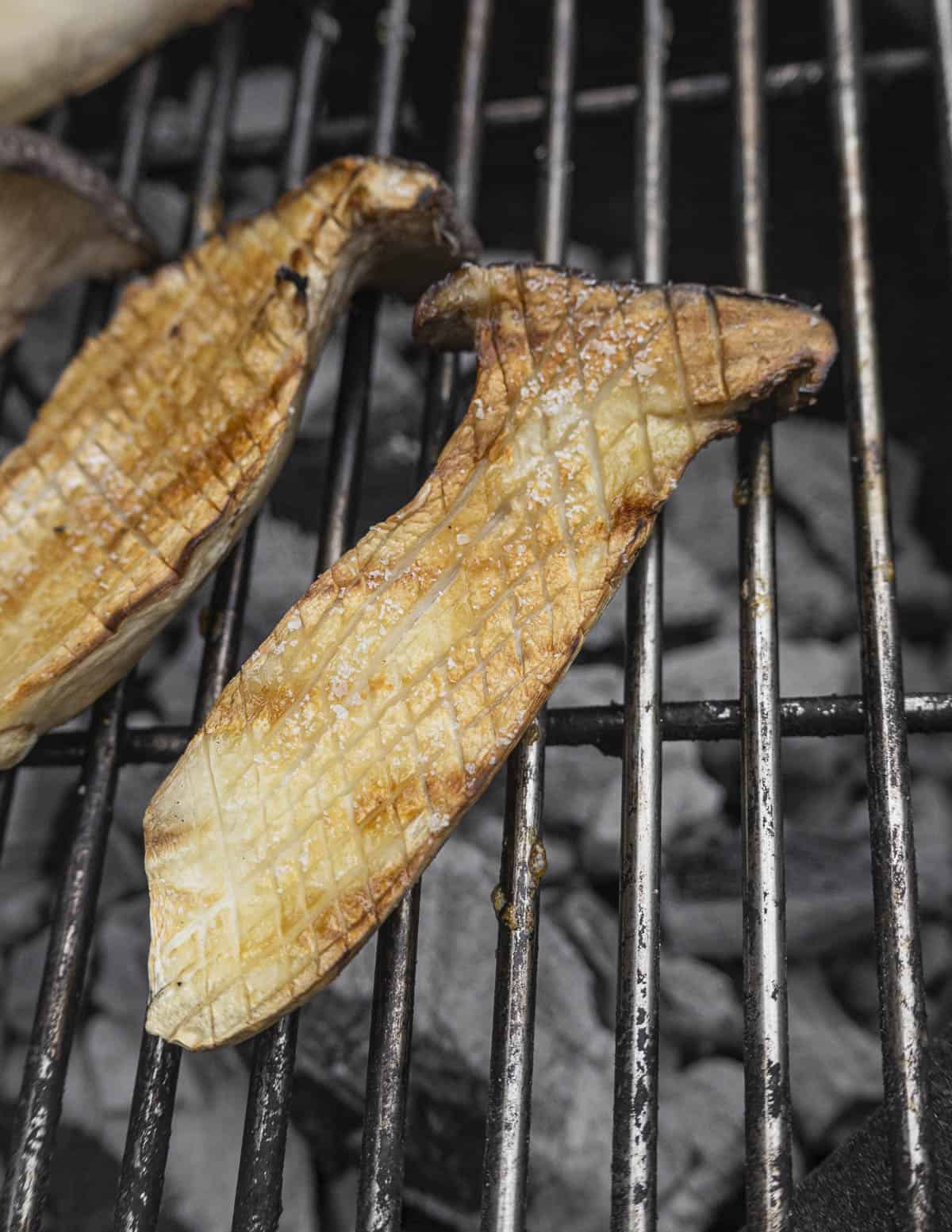 Grilling king oyster mushrooms that have been cut and scored showing the uneven caramelization. 