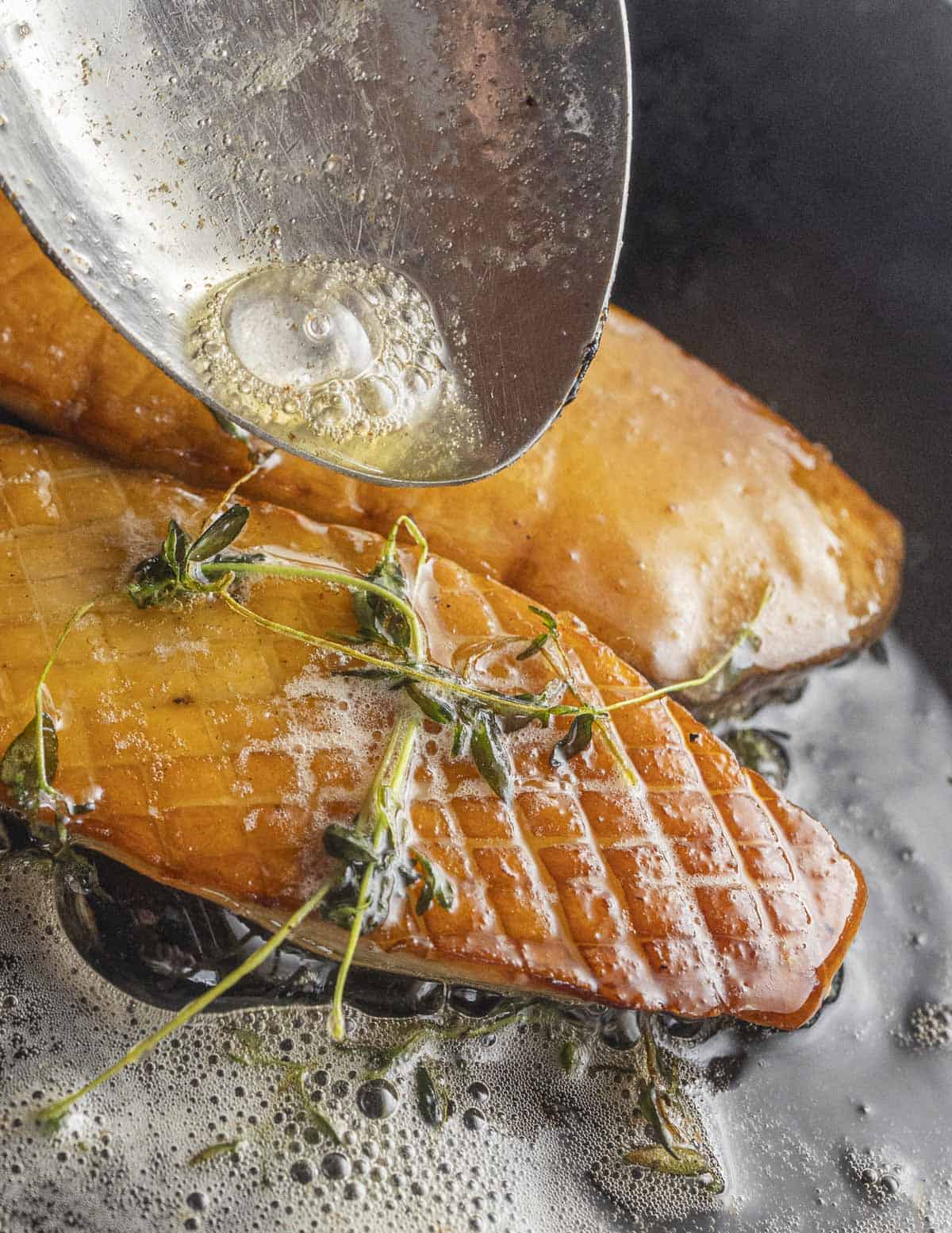 A spoon drizzling melted butter over a golden brown slice of king oyster mushroom.