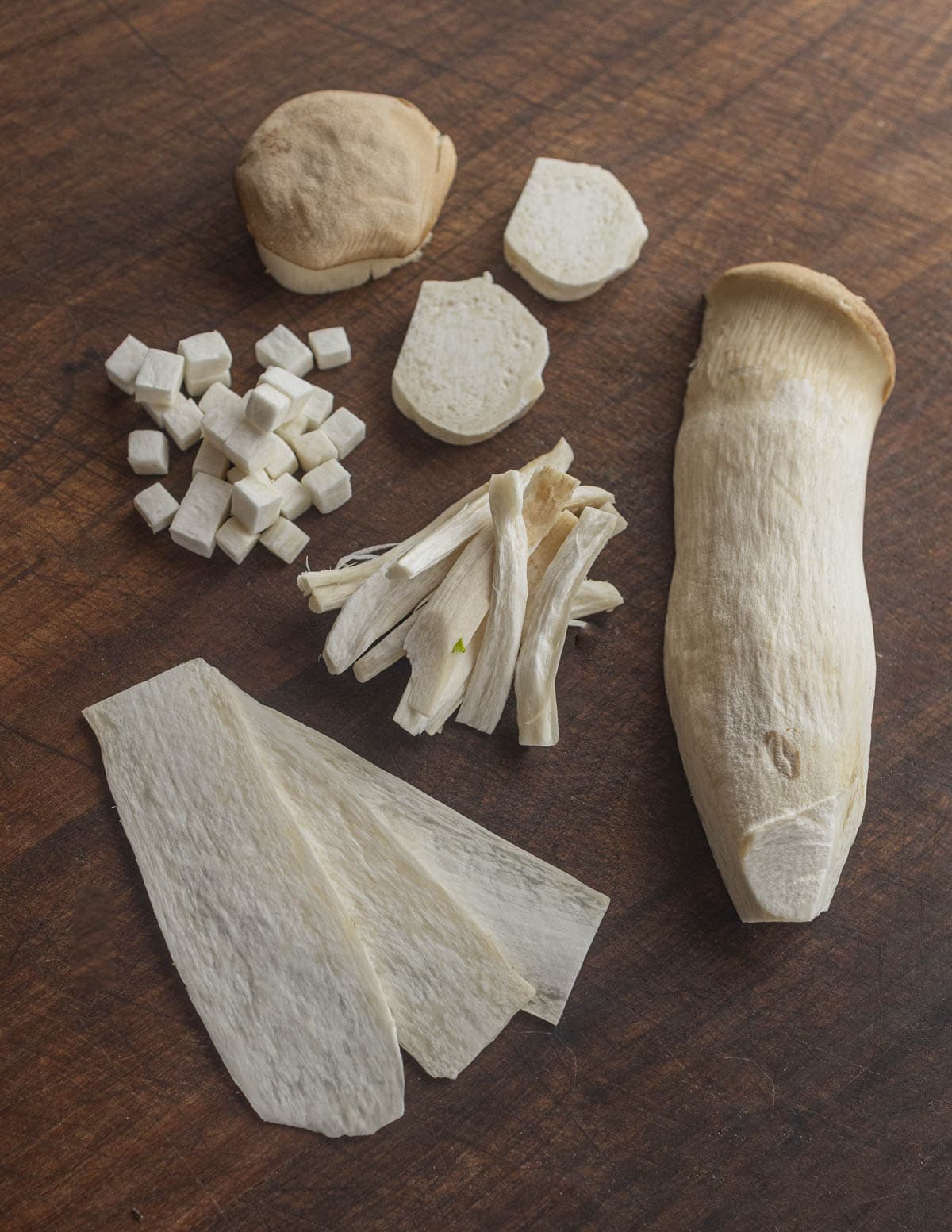 King trumpet or king oyster mushrooms cut into many different shapes on a cutting board. 