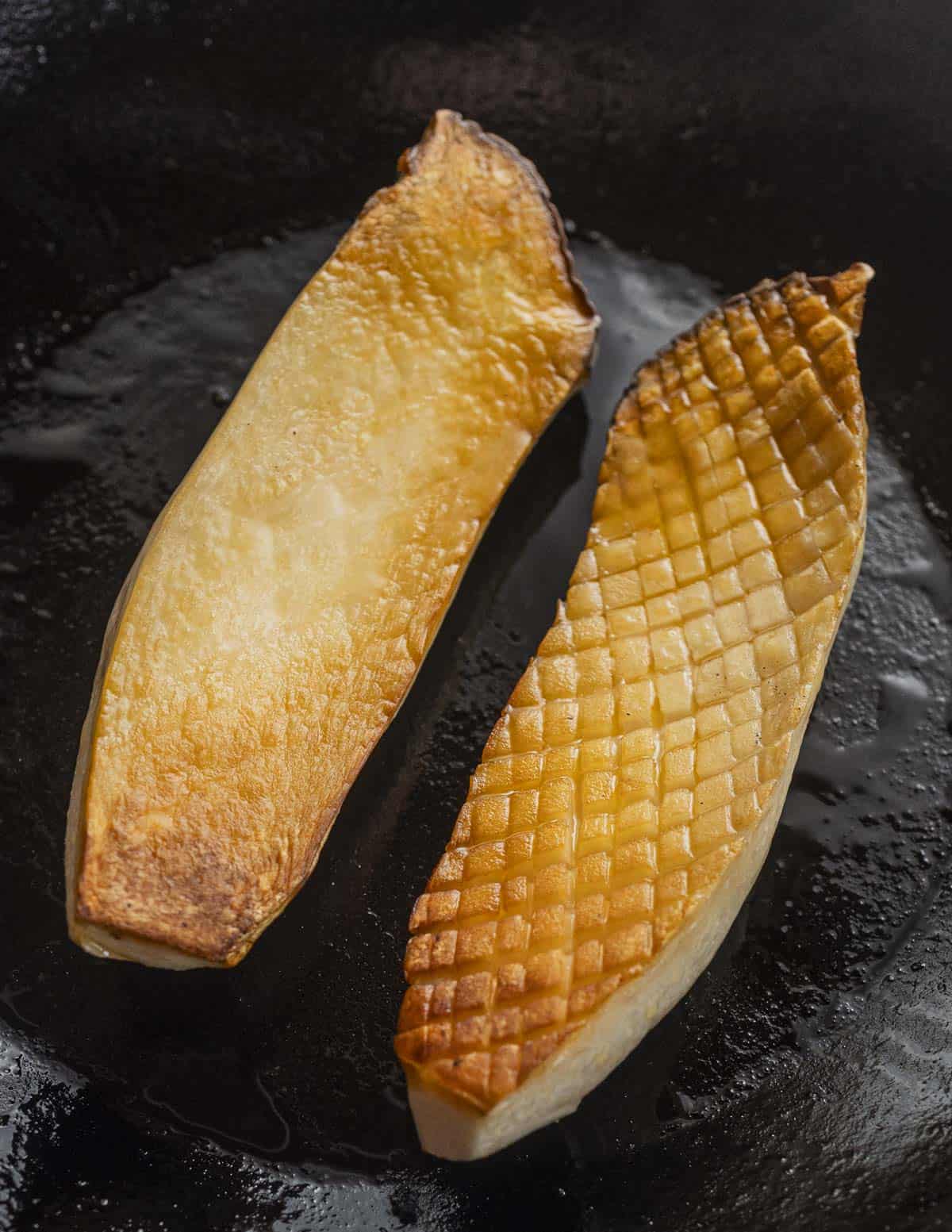 Two cut and seared king oyster mushrooms, one scored with a cross hatch pattern to show differences in how the mushrooms sear. 