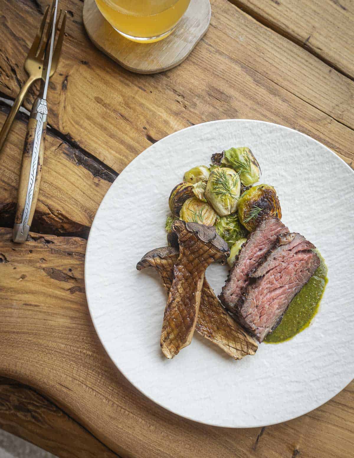 A sliced bavette steak with dill  sauce and brussels sprouts with grilled king oyster mushrooms. 