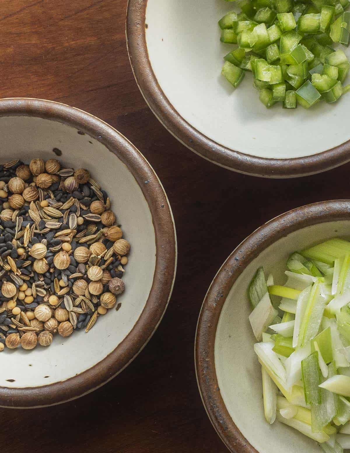 Three different bowls filled with herbs, onions, spices and chopped chili for garnishing missi roti flatbreads. 