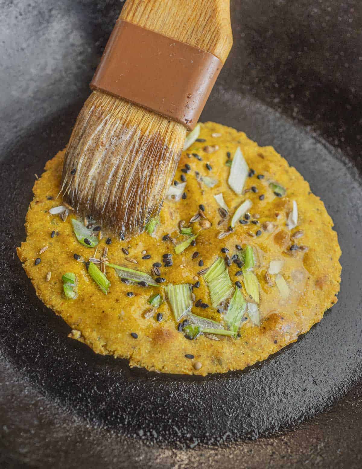 Brushing a cooked chickpea flatbread with melted garlic butter. 