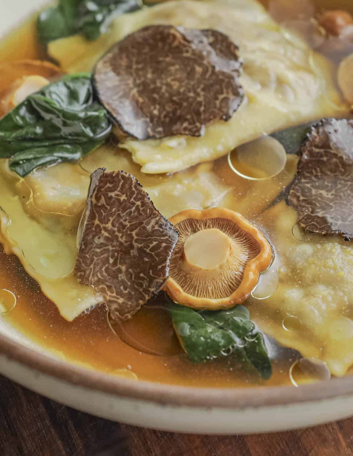 A bowl of porcini ravioli with truffle slices, chanterelles and spinach. 