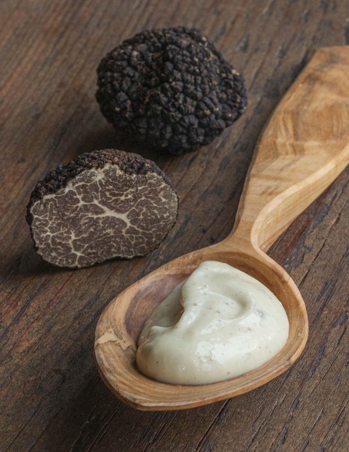 Black truffles surrounding a spoon filled with black truffle aioli. 