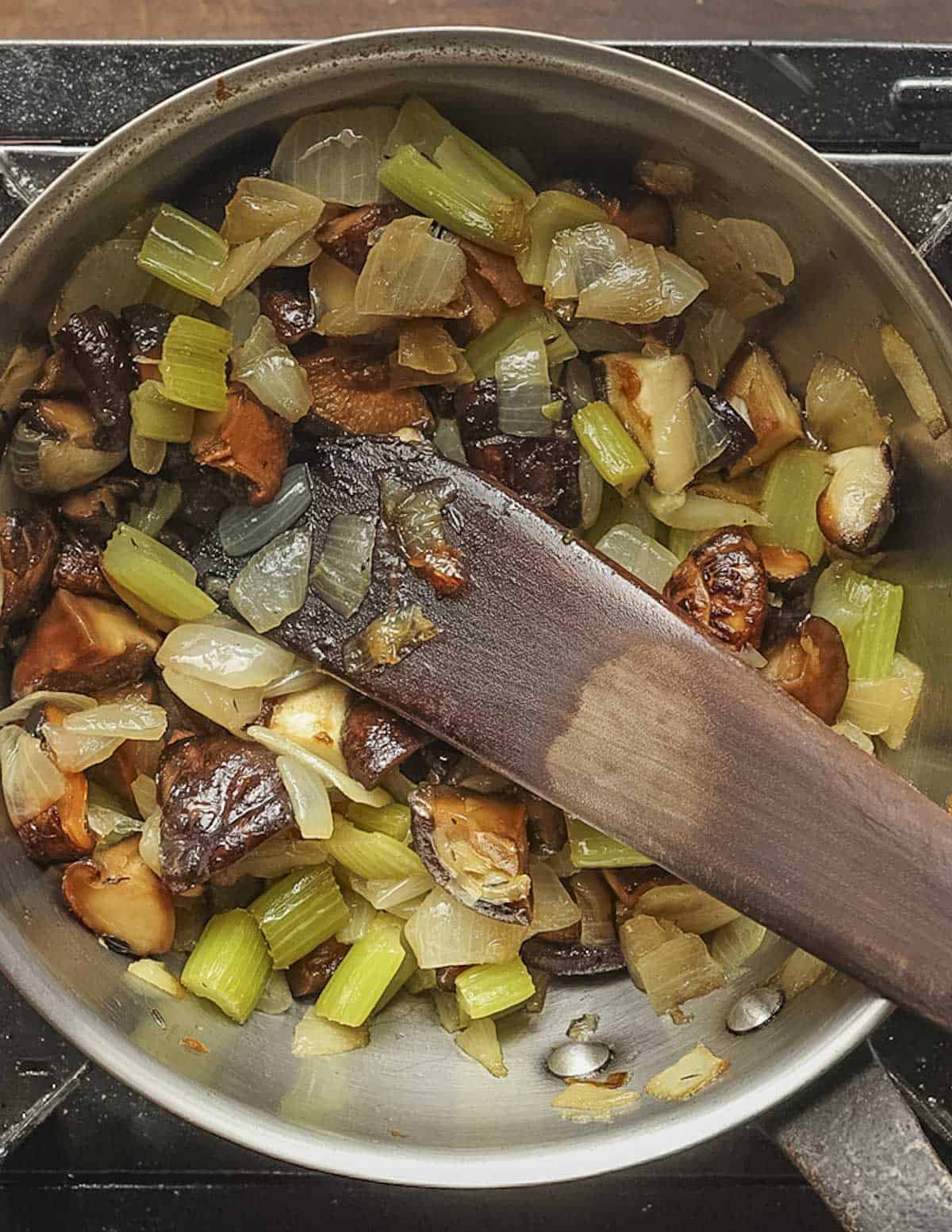 Adding roasted shiitake mushrooms to a pot of vegetables for soup. 